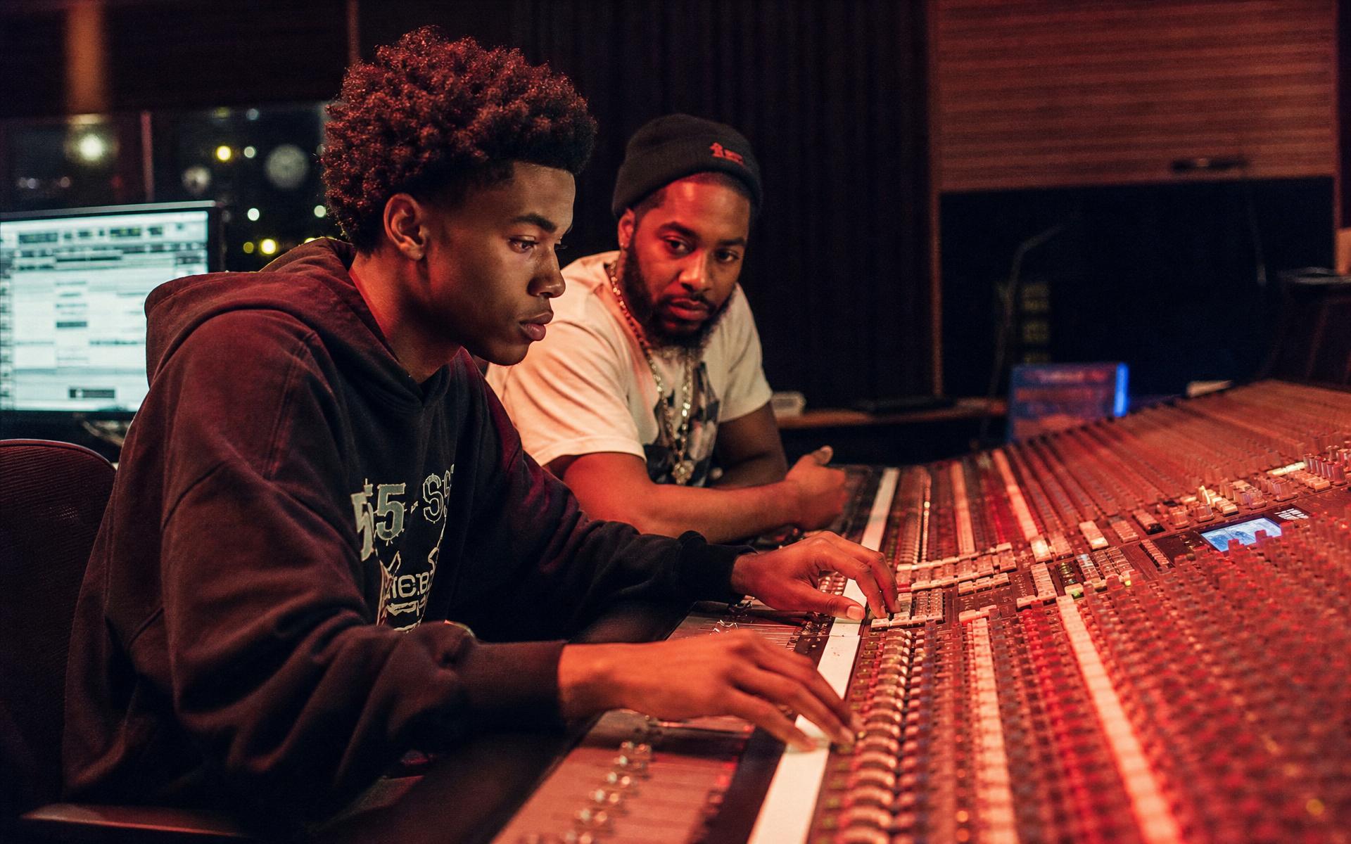 Young producer and mentor at a recording console, lit in red